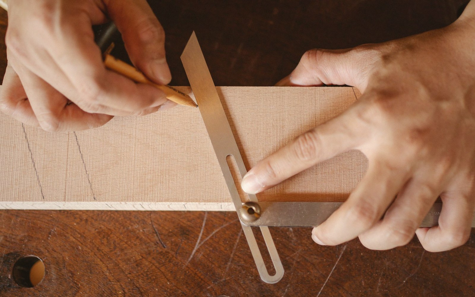 Hands using a bevel gauge to mark angled lines on a wooden board