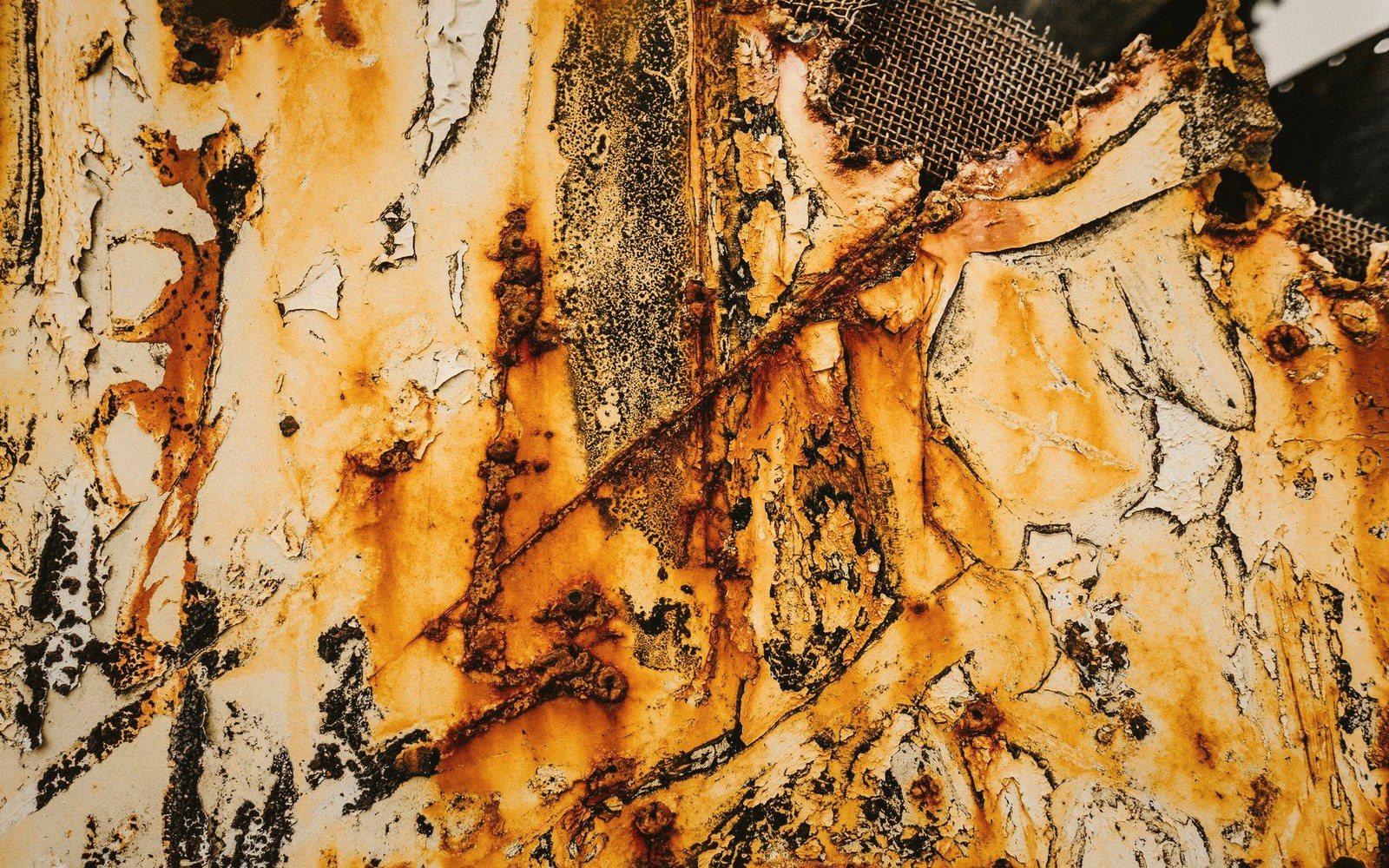 Rust and peeling paint cover corroded metal in streaks of orange and black