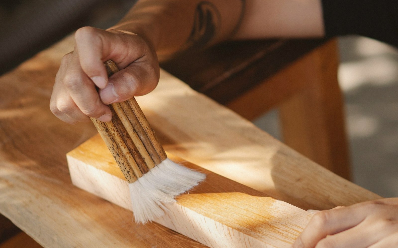 A hand applies wood stain or varnish to a plank with a brush