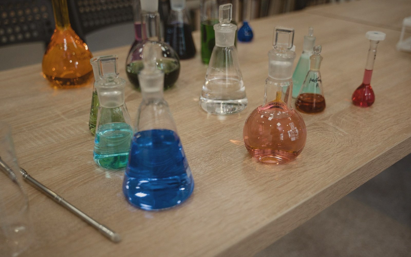 Glass flasks filled with brightly colored liquids arranged on a wooden table