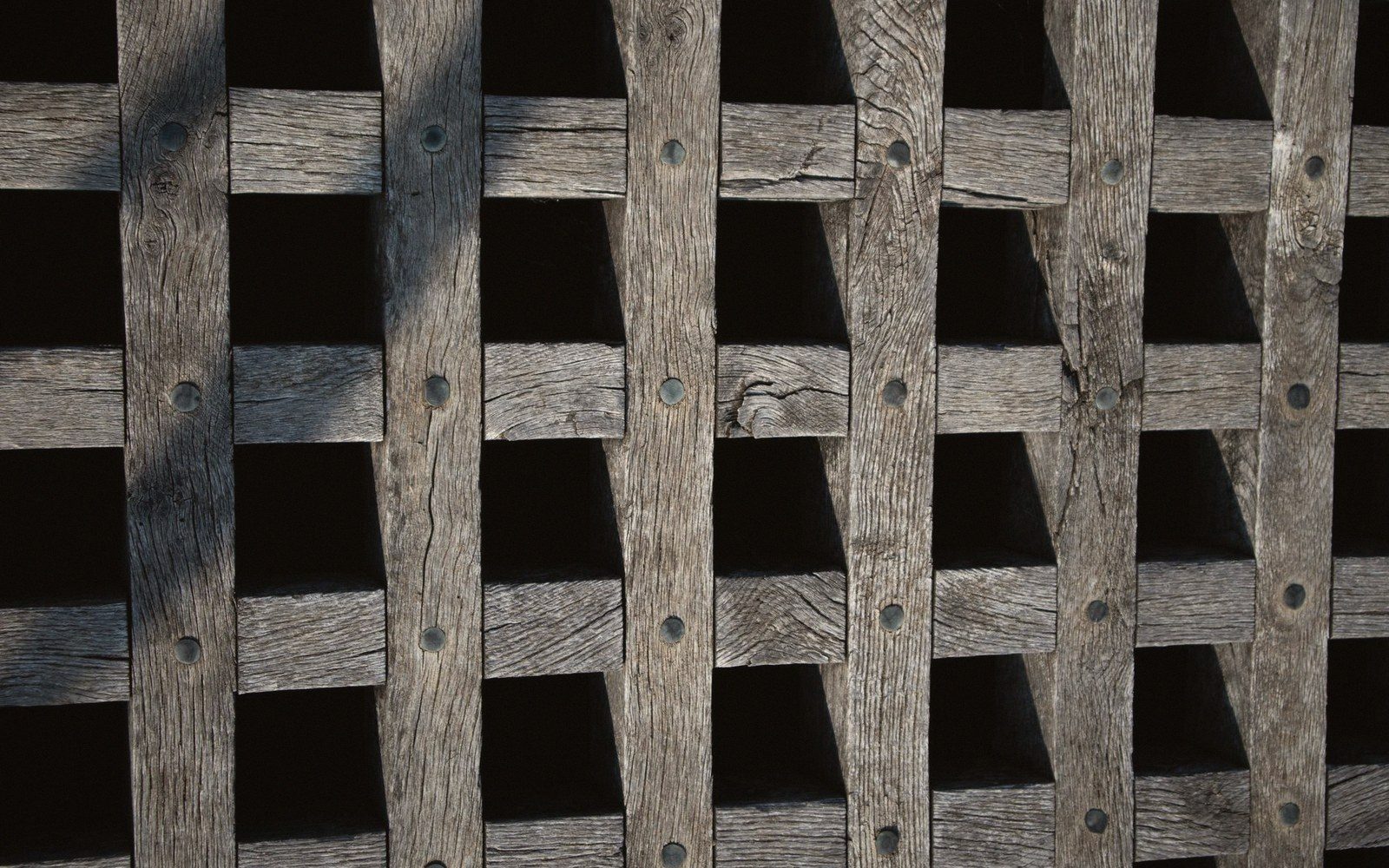 Weathered wooden lattice with crisscrossing slats and visible nail heads
